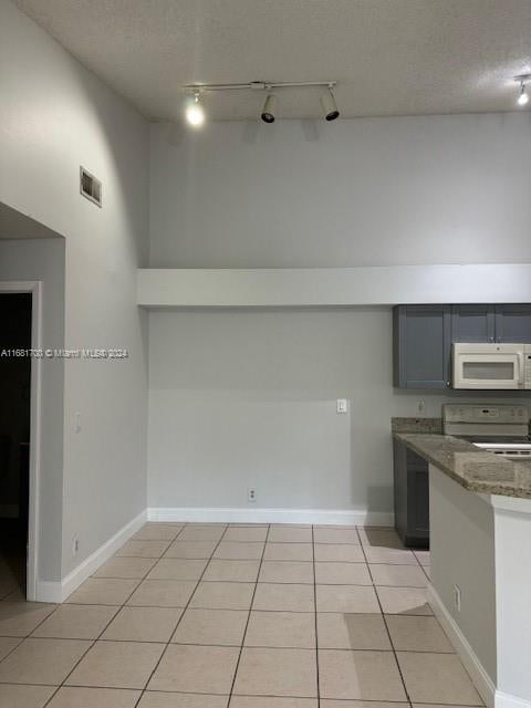 kitchen with light tile patterned flooring, a textured ceiling, white appliances, and dark stone countertops