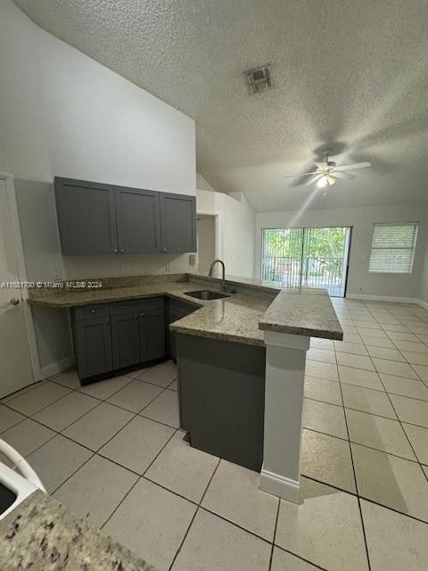 kitchen featuring kitchen peninsula, sink, light tile patterned flooring, vaulted ceiling, and a textured ceiling