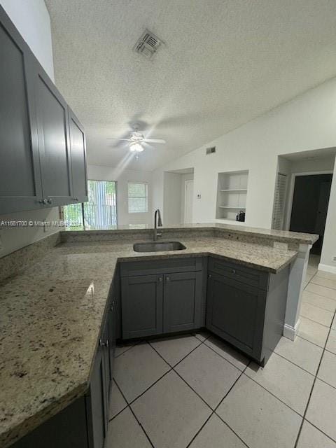 kitchen featuring lofted ceiling, kitchen peninsula, light tile patterned floors, a textured ceiling, and sink