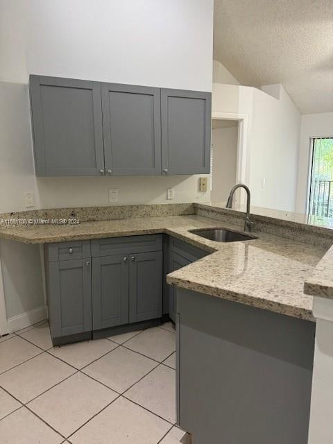 kitchen featuring gray cabinetry, sink, vaulted ceiling, light stone counters, and a textured ceiling