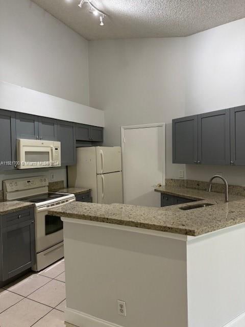 kitchen featuring white appliances, light stone countertops, sink, a textured ceiling, and kitchen peninsula