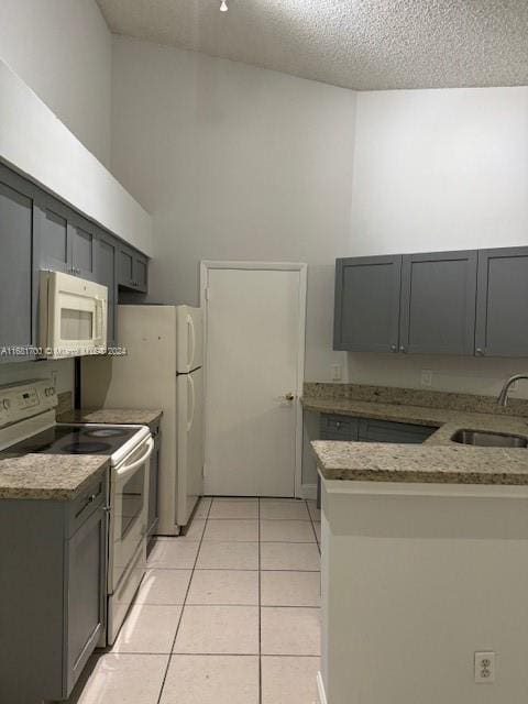 kitchen with gray cabinetry, sink, light tile patterned flooring, a textured ceiling, and white appliances