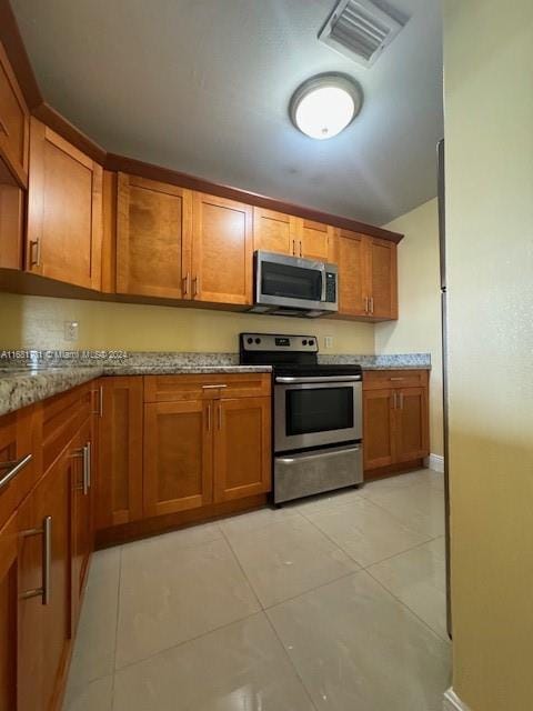 10018 NW 4th St Unit 203, Pembroke Pines, FL 33024 - kitchen with appliances with stainless steel finishes, brown cabinets, light stone countertops, and light tile patterned floors