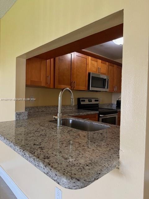 10018 NW 4th St Unit 203, Pembroke Pines, FL 33024 - kitchen with stainless steel appliances, a peninsula, light stone countertops, and brown cabinets