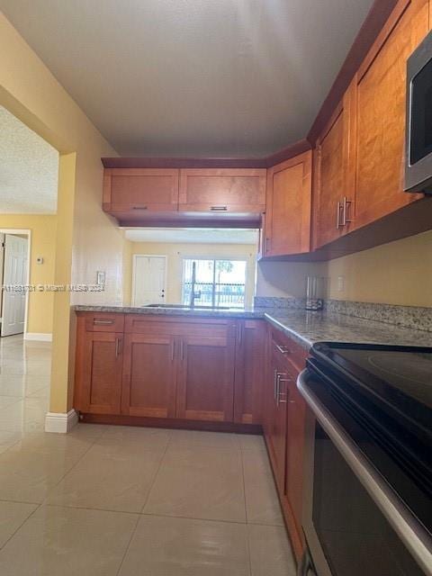 10018 NW 4th St Unit 203, Pembroke Pines, FL 33024 - kitchen with stainless steel appliances, light tile patterned flooring, brown cabinetry, and light stone counters
