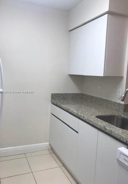 kitchen with sink, white cabinets, dark stone counters, and light tile patterned floors