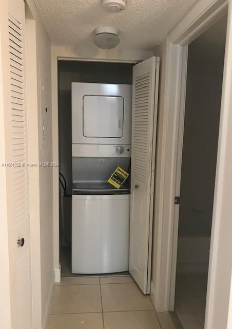 clothes washing area with stacked washing maching and dryer, a textured ceiling, and light tile patterned floors