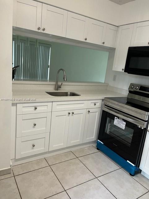 kitchen with a textured ceiling, white cabinets, stainless steel appliances, and light tile patterned floors