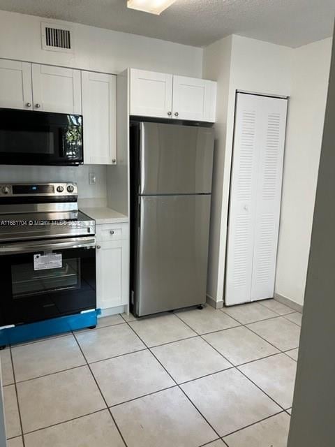 kitchen featuring white cabinetry, stainless steel appliances, light tile patterned flooring, and a textured ceiling