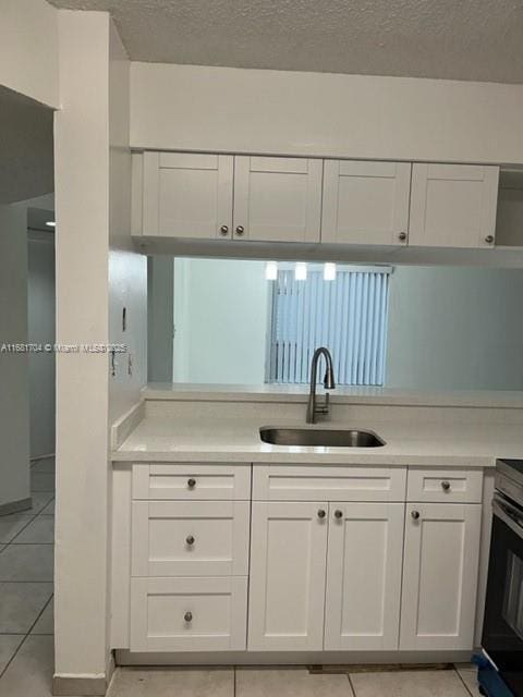 kitchen with sink, light tile patterned floors, white cabinets, and a textured ceiling