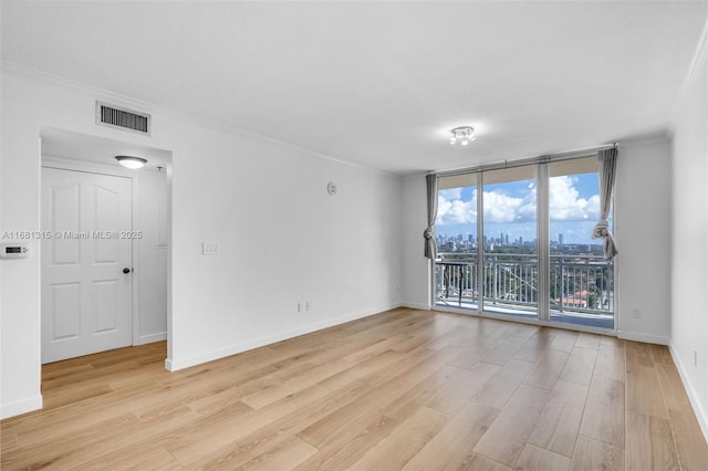 empty room featuring a wall of windows, visible vents, light wood-style floors, and baseboards