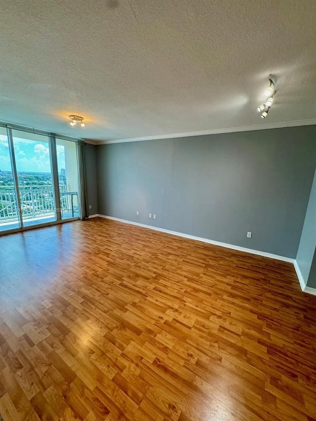 spare room with a textured ceiling, ornamental molding, light wood-type flooring, and a wall of windows