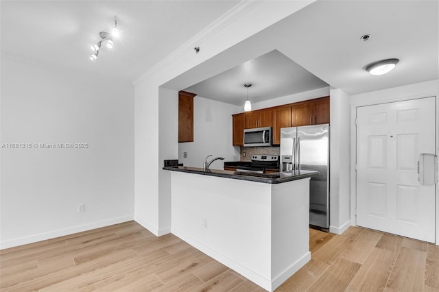 kitchen featuring stainless steel appliances, a peninsula, brown cabinetry, dark countertops, and decorative light fixtures