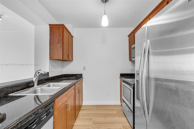 kitchen with stainless steel appliances, a sink, light wood-style floors, hanging light fixtures, and brown cabinets