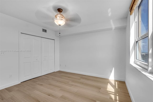 unfurnished bedroom with a closet, visible vents, light wood-style flooring, a ceiling fan, and baseboards
