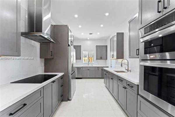 kitchen featuring gray cabinets, light tile patterned flooring, appliances with stainless steel finishes, sink, and wall chimney range hood