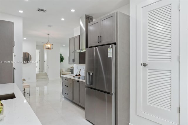 kitchen featuring wall chimney exhaust hood, decorative light fixtures, stainless steel fridge with ice dispenser, a notable chandelier, and light stone countertops