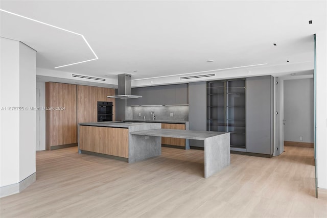 kitchen featuring backsplash, ventilation hood, light hardwood / wood-style floors, double oven, and a kitchen island