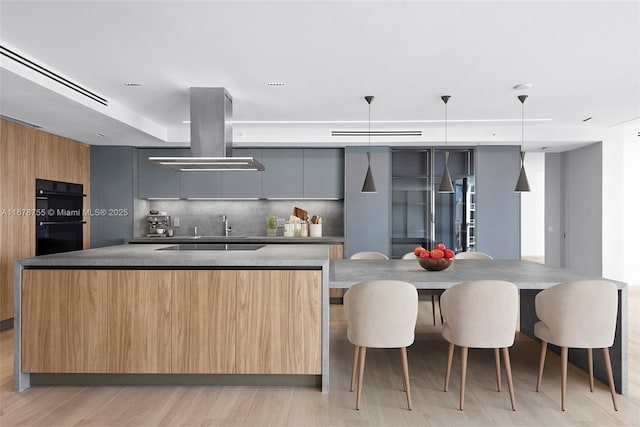 kitchen with a large island, dobule oven black, modern cabinets, and island range hood