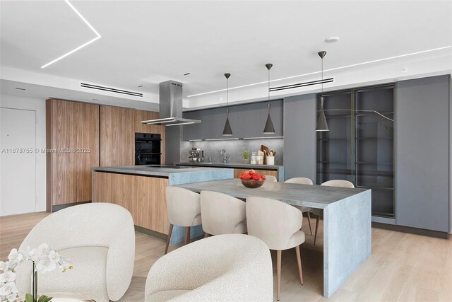 kitchen with black double oven, a center island, pendant lighting, island exhaust hood, and backsplash