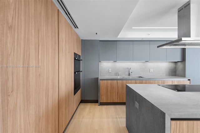 kitchen featuring island range hood, sink, backsplash, light hardwood / wood-style floors, and black appliances