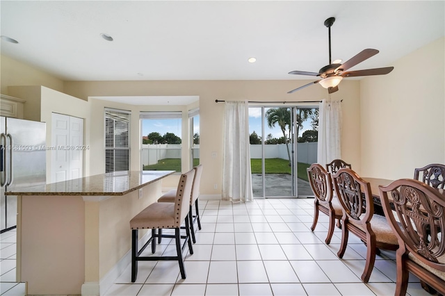 kitchen featuring a breakfast bar area, ceiling fan, dark stone counters, stainless steel refrigerator, and light tile patterned flooring