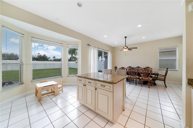 kitchen featuring cream cabinets, ceiling fan, a kitchen island, light stone countertops, and light tile patterned flooring