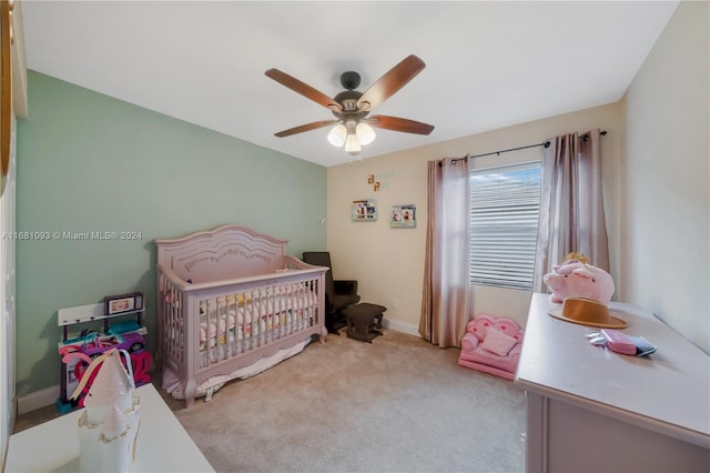 bedroom featuring a nursery area, light carpet, and ceiling fan