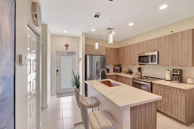 kitchen with appliances with stainless steel finishes, sink, hanging light fixtures, a breakfast bar area, and an island with sink