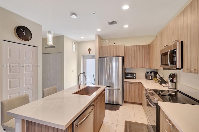 kitchen featuring a kitchen island with sink, sink, light tile patterned floors, decorative light fixtures, and stainless steel appliances