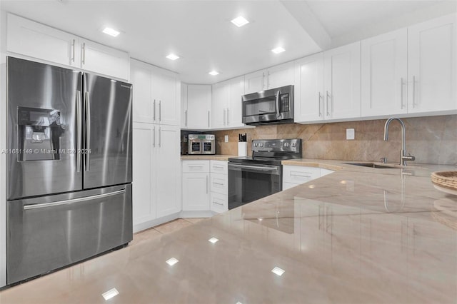 kitchen with stainless steel appliances, backsplash, sink, light stone countertops, and white cabinetry