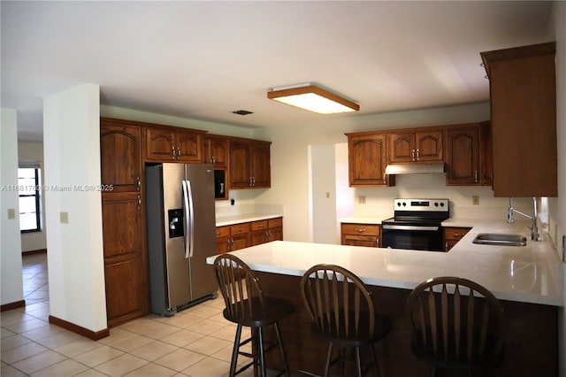 kitchen with appliances with stainless steel finishes, a peninsula, light countertops, under cabinet range hood, and a sink