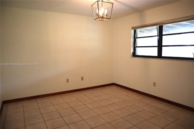 empty room with a notable chandelier, light tile patterned flooring, and baseboards