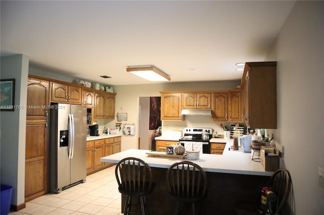 kitchen with appliances with stainless steel finishes, light tile patterned floors, kitchen peninsula, and a kitchen bar