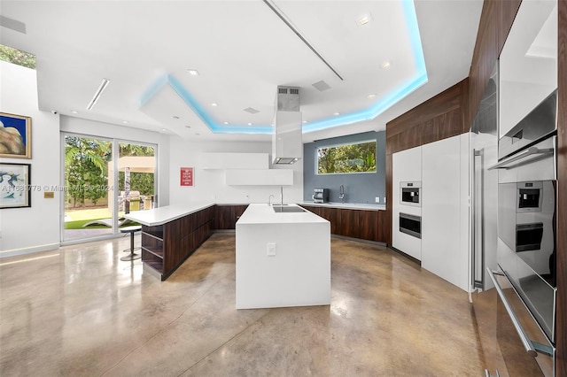 kitchen with dark brown cabinetry, oven, a raised ceiling, and a kitchen island with sink