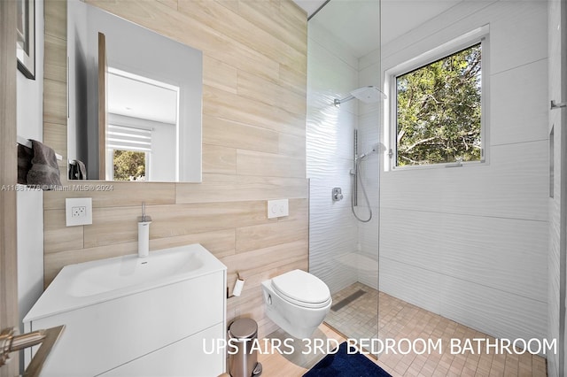 bathroom featuring a tile shower, vanity, tile walls, and toilet