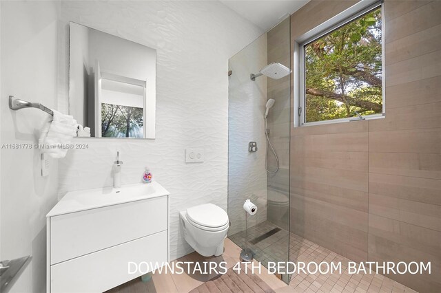 bathroom featuring toilet, a tile shower, tile walls, and vanity