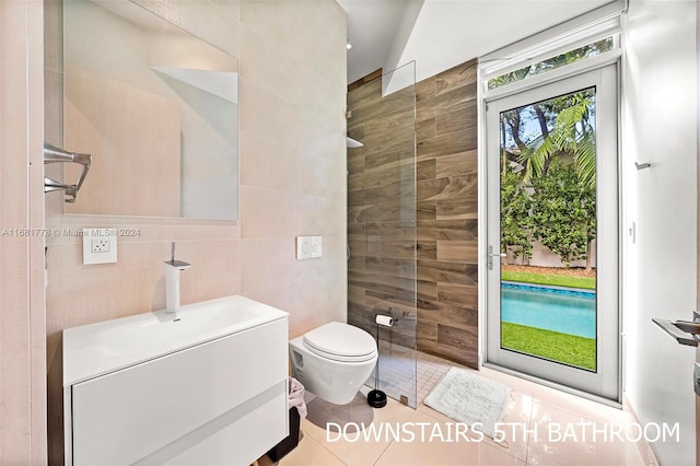 bathroom featuring a tile shower, tile patterned flooring, toilet, vanity, and tile walls