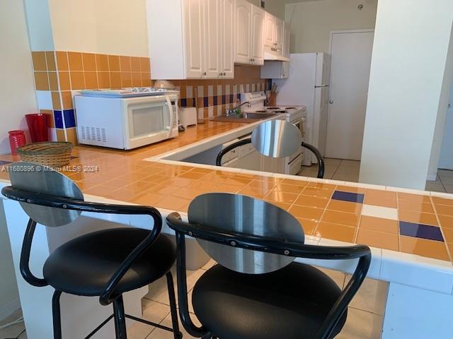 kitchen featuring light tile patterned floors, tile countertops, white cabinetry, decorative backsplash, and a breakfast bar area