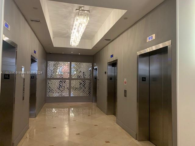 hall featuring elevator, a tray ceiling, and an inviting chandelier