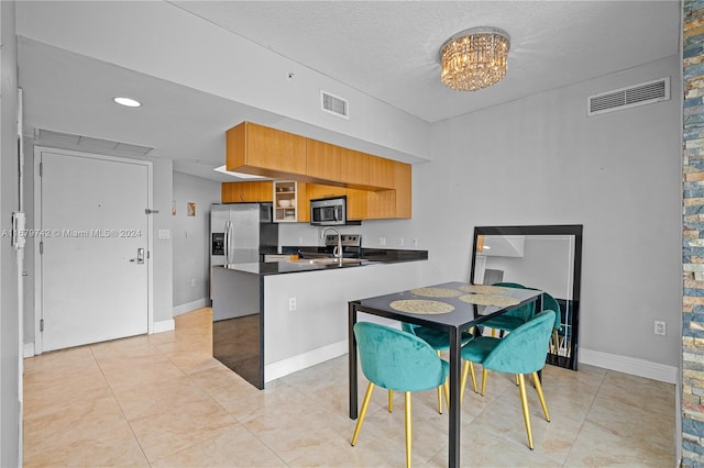 kitchen with sink, a textured ceiling, kitchen peninsula, stainless steel appliances, and an inviting chandelier