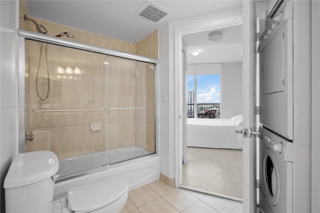 bathroom with tile patterned flooring, shower / bath combination with glass door, toilet, and stacked washing maching and dryer