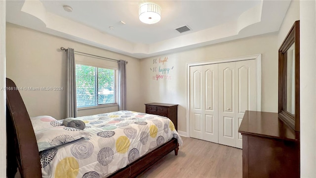 bedroom featuring light hardwood / wood-style floors, a closet, and a tray ceiling