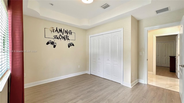 unfurnished bedroom with a closet, light wood-type flooring, and a raised ceiling