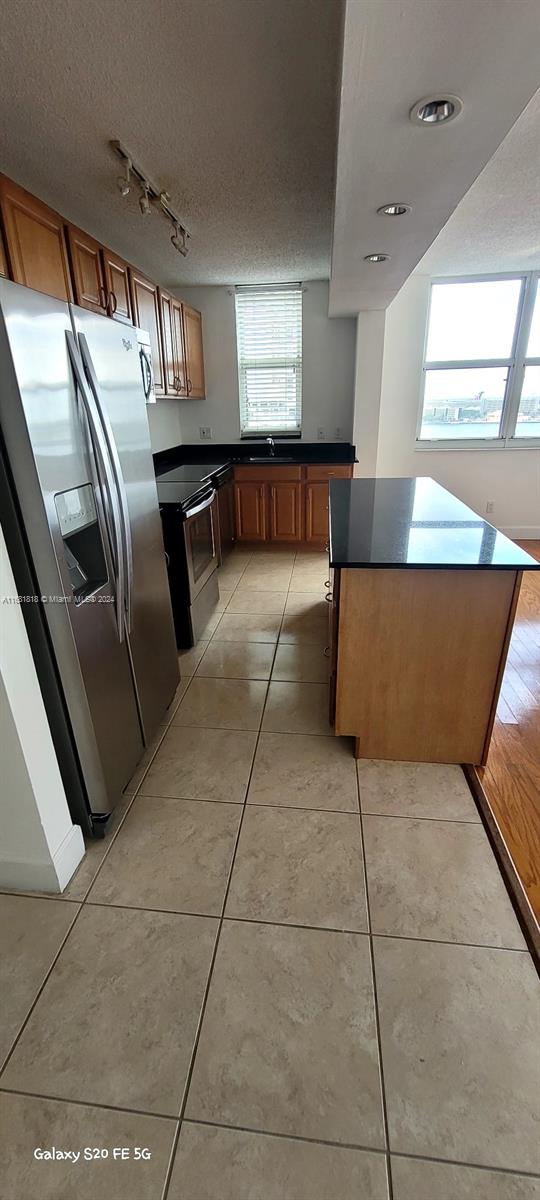 kitchen with stainless steel refrigerator with ice dispenser, a textured ceiling, light tile patterned floors, and a wealth of natural light