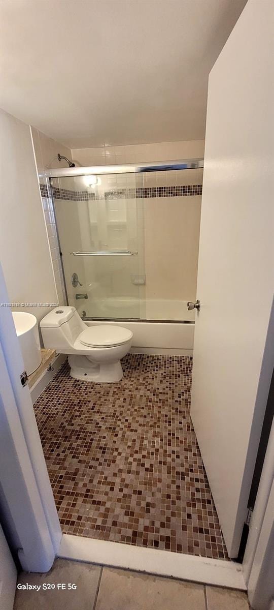 bathroom featuring toilet, tile patterned floors, and enclosed tub / shower combo