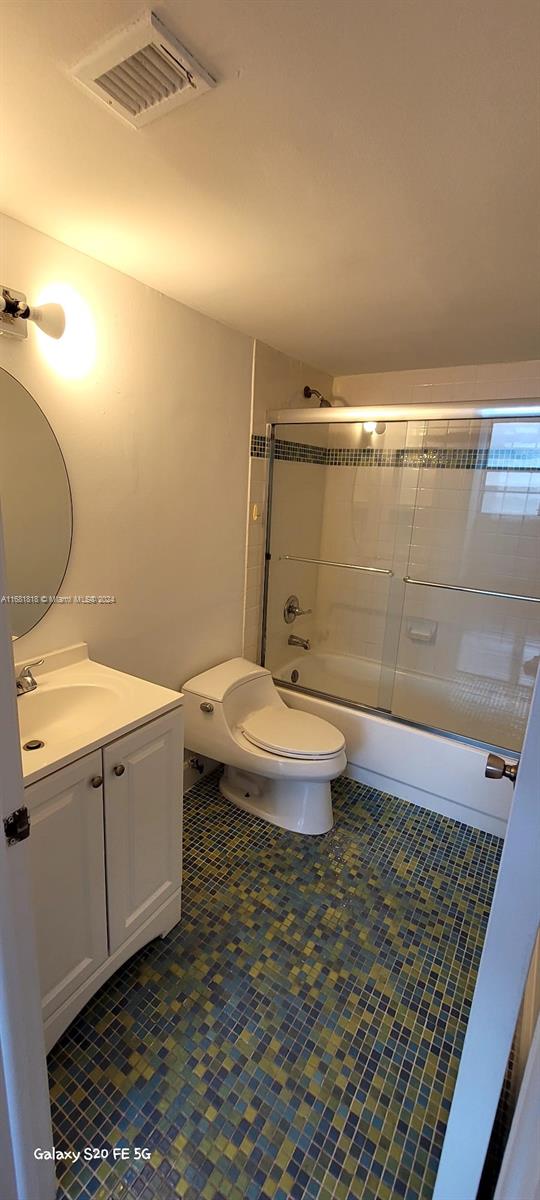 full bathroom with vanity, bath / shower combo with glass door, toilet, and tile patterned flooring