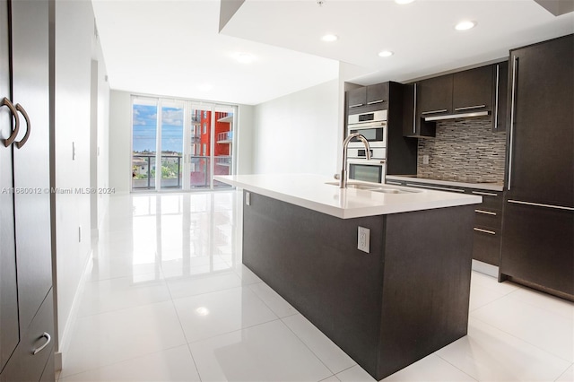 kitchen with tasteful backsplash, a center island with sink, light tile patterned flooring, sink, and stainless steel double oven