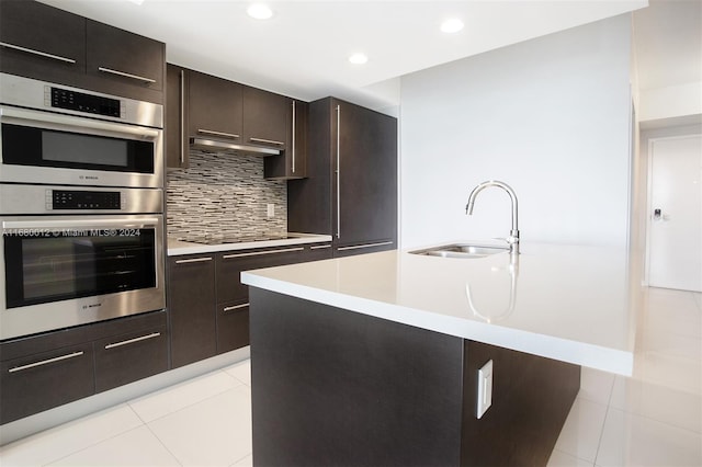 kitchen featuring sink, stainless steel double oven, an island with sink, and light tile patterned floors