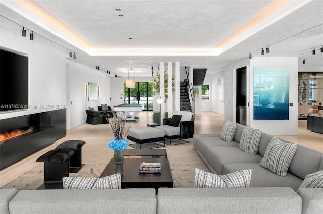 living room with track lighting, light wood-type flooring, and a raised ceiling